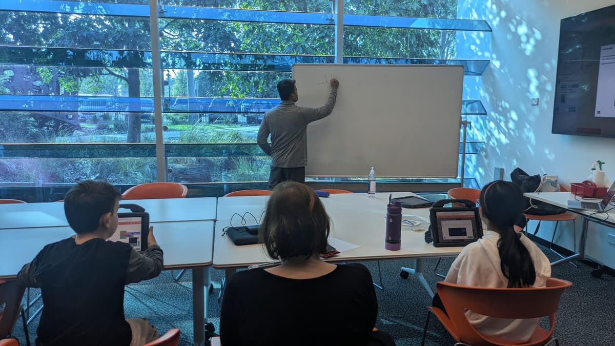 Kids watching a whiteboard explanation during a ThinkerLab game coding class