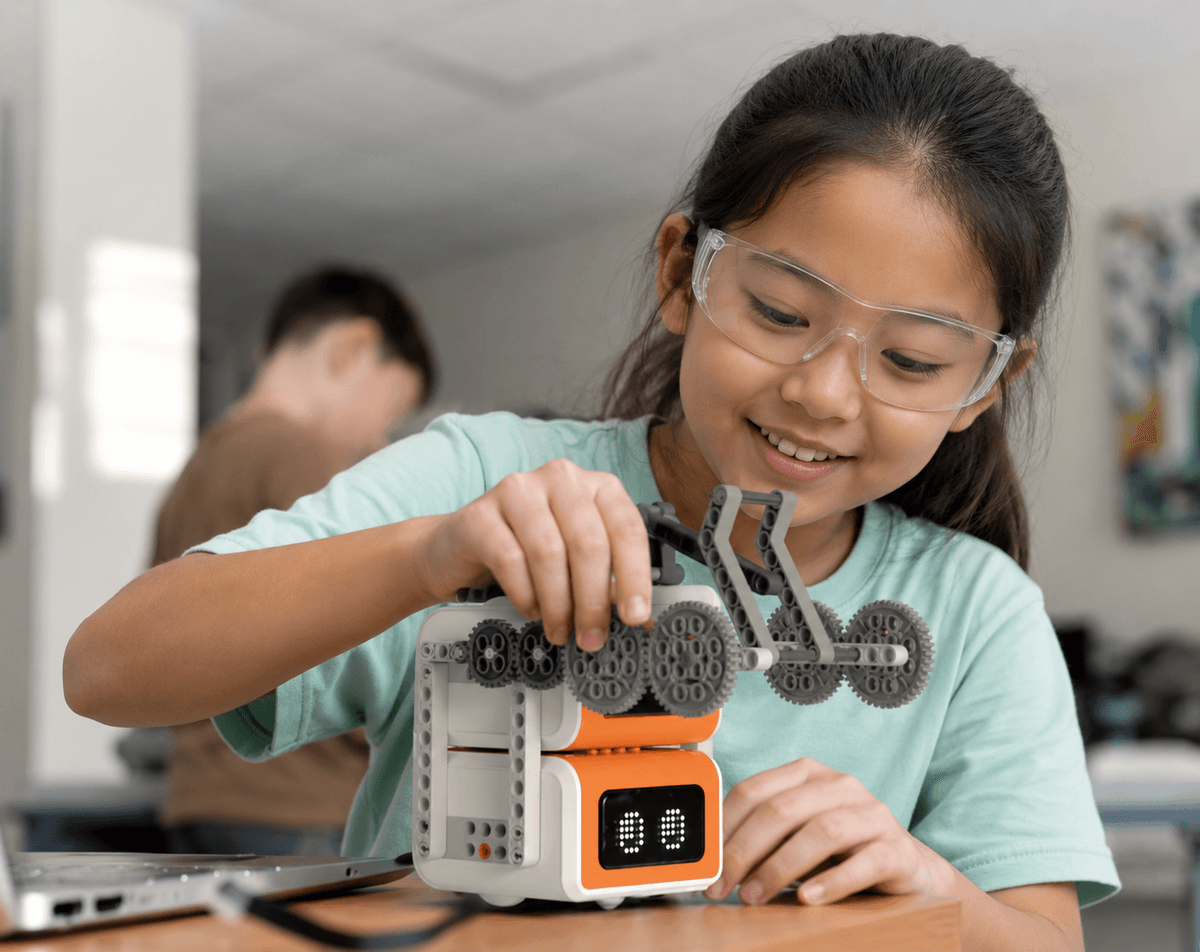 A girl in safety goggles building and coding a geared robot in a ThinkerLab term class